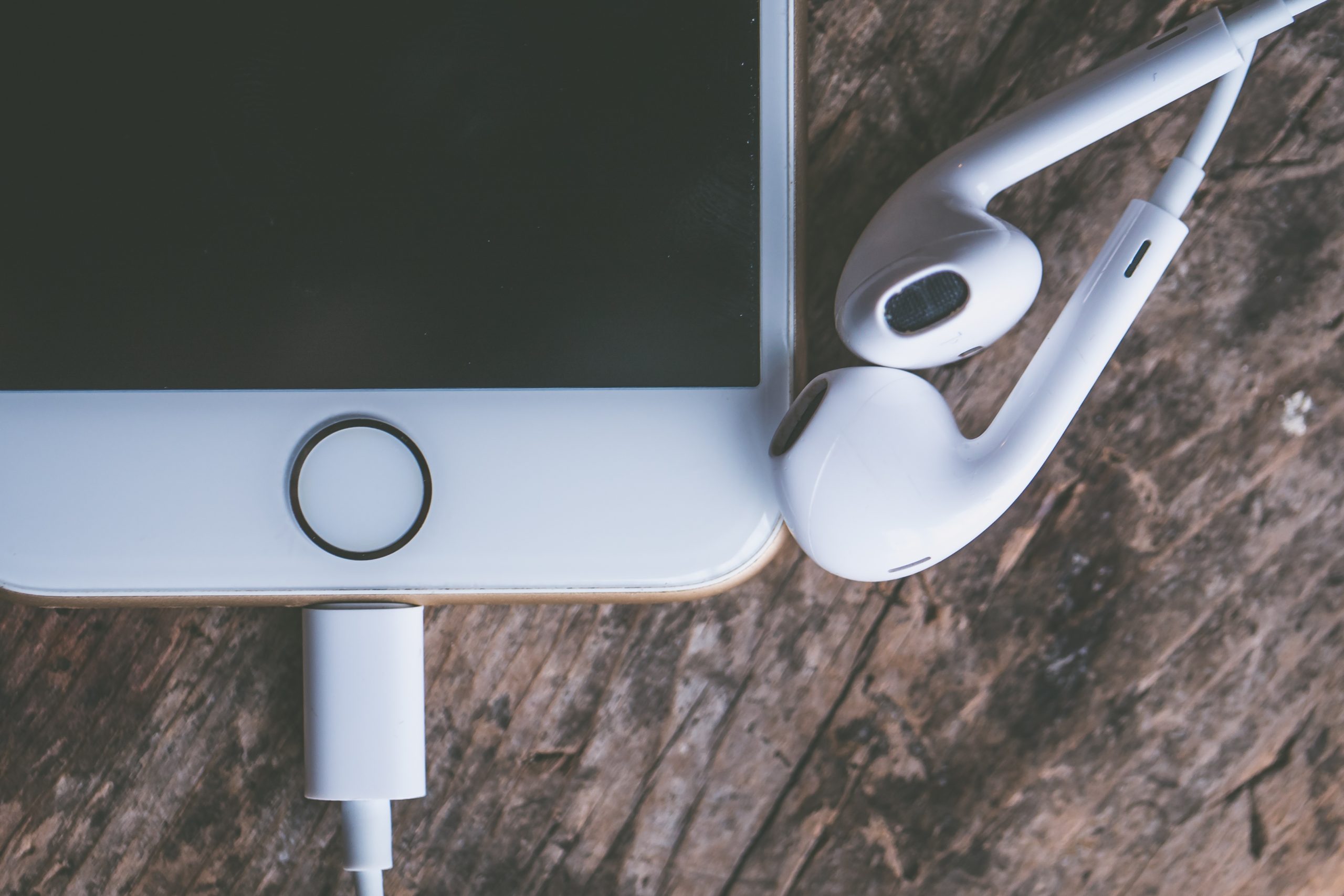 A closeup shot of a smartphone with connected headphones on a wooden surface